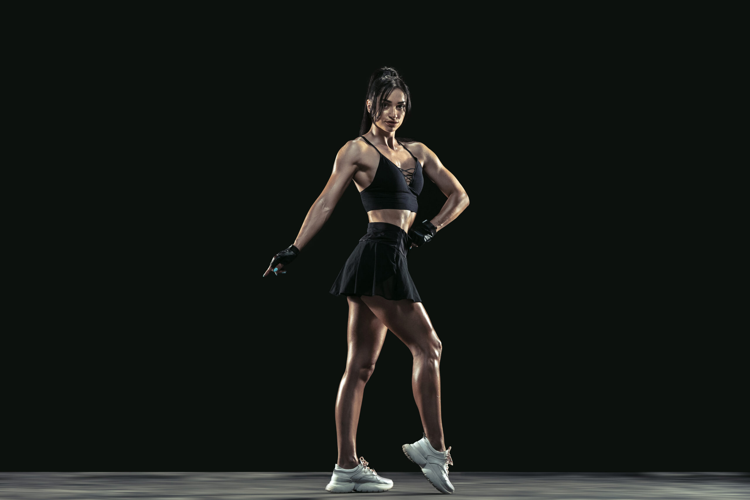 Beautiful young female athlete practicing on black studio background, full length portrait. Sportive fit brunette model posing confident. Body building, healthy lifestyle, beauty and action concept.